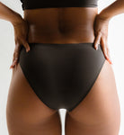 Rear view of a model wearing Pretty Kitty Klub Briefkini in Kitty Noir black, showing the fit and back coverage.